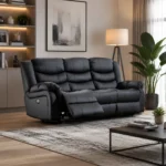A stylish black leather power-reclining sofa placed in a modern, sophisticated living room featuring hardwood flooring, an abstract wall art piece, illuminated built-in shelving, a floor lamp, and a large indoor potted plant.