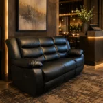 A sleek black leather recliner sofa placed on a patterned rug in a sophisticated, dimly lit lounge or restaurant waiting area featuring moody accent lighting and dark textured walls.